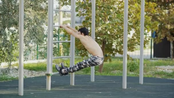 El atleta en el campo de deportes se calienta antes del entrenamiento. Un hombre musculoso va a practicar deportes al aire libre. El tipo con pantalones del ejército hace los ejercicios. Entrenamiento conceptual, crossfit, fitness, saludable . — Vídeos de Stock