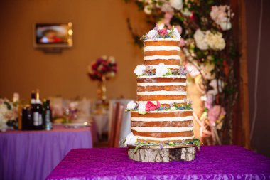 Çok düzeyli beyaz düğün pastası çiçeklerle süslenmiş bir masada duruyor. Yemek, tatlılar ve tatlılar bir partide kavramı.