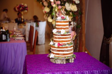 Çok düzeyli beyaz düğün pastası çiçeklerle süslenmiş bir masada duruyor. Yemek, tatlılar ve tatlılar bir partide kavramı.