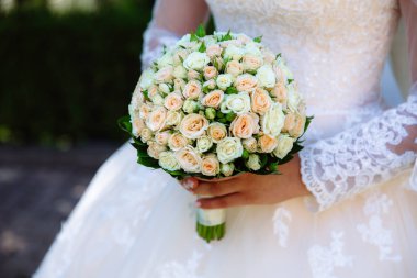 Kırpılan düğün çerçeve bir close-up ihale buket gül gelinin elinde olduğunu. Bir kız bir gelinlik çiçekleri tutuyor.