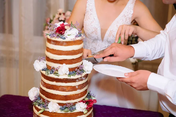 Primer plano novia y novio manos corte multinivel pastel de boda blanco decorado con flores se encuentra en una mesa. Concepto de comer, dulces y postres en una fiesta . — Foto de Stock