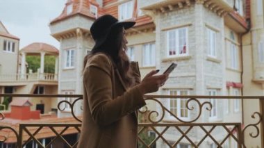 Yakın çekim, güzel bir Avrupa kadın Avrupa şehir etrafında yürür, moda giysiler giyer, şık görünüyor, eski bir tuğla ev karşı duruyor, arkadaşı için Sms yazıyor, onu köprüde bekler