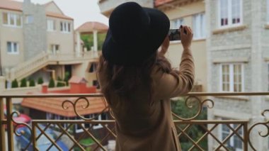 Arka görünümünden, yakın çekim, ince kadın palto ve şapka şehir etrafında yürür, onun Smartphone'da mimar bir fotoğrafı çeker, bir yürüyüş sahiptir. Kızım hafta sonu Avrupa'ya uçtu..