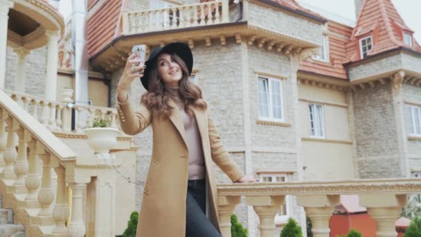 Close-up a young girl walks outside on an excursion, photographed on a balcony against the background of an old European city. A woman makes a photo on her smartphone, sending air kisses. — Stock Video