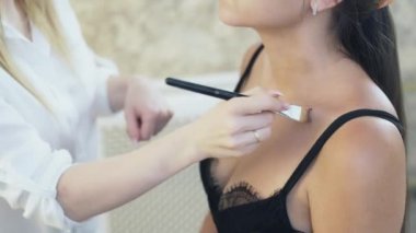 Makyöz kadeh kırpılmış yakın çekim koyar sesi istemcileri yüz, boyun ve dekolte. Makyaj, onun tonunu dengeler bir etkinlik için onu stilist, iri göğüslü genç bir kız geldi.