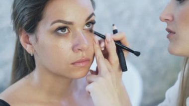 Yakın çekim steadicam. Esmer modeli bir güzellik stüdyoda oturmuş, o bir profesyonel, yapar dumanlı gözler tarafından göz makyajı yapıyor. Karanlık gölgeler ile alt ve üst göz kapaklarında makyaj sanatçısı boyalar