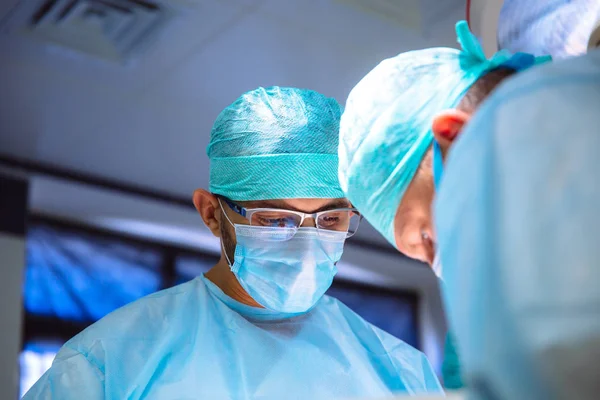 Dois médicos do sexo masculino em roupas médicas estéreis realizam uma operação em um hospital. A equipe profissional trabalha em uma clínica, um cirurgião com um assistente. O conceito de saúde, medicina . — Fotografia de Stock