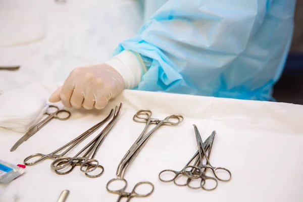 Nahaufnahme chirurgischer Instrumente auf einem medizinischen Tisch in einer Klinik während der Operation. Sterile Metallschere, Klammer, chirurgische Nadel am Tisch oder in der Arzthand. das Konzept der Gesundheit, Werkzeuge. — Stockfoto