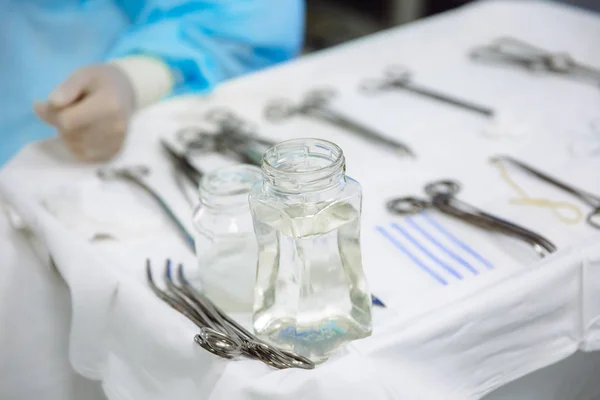 Instrumentos cirúrgicos de close-up em uma mesa médica em uma clínica durante a cirurgia. Tesoura estéril de metal, braçadeira, agulha cirúrgica na mesa ou na mão do médico. O conceito de saúde, ferramentas . — Fotografia de Stock