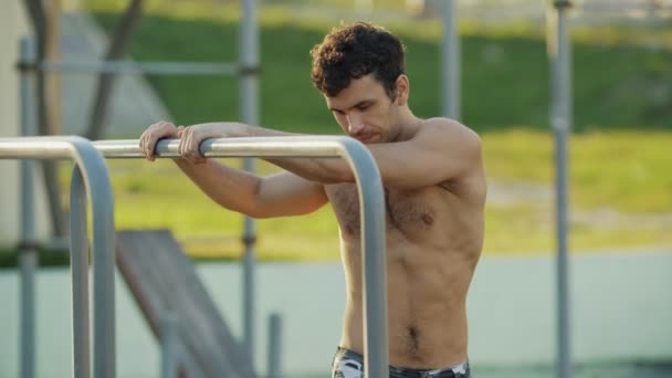 El atleta en el campo de deportes se calienta antes del entrenamiento. Un hombre musculoso va a practicar deportes al aire libre. El tipo con pantalones del ejército hace los ejercicios. Entrenamiento conceptual, crossfit, fitness, saludable . — Vídeo de stock