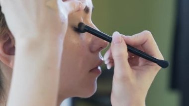 Yakın çekim çerçeve, ağır çekim kırpılmış. Makyaj sanatçısı bir kalem ve bir fırça ile pigment gölgelendirme kızla boyar. Çalışma sonucu değerlendirmek için gözlerini açmak için model istekler.