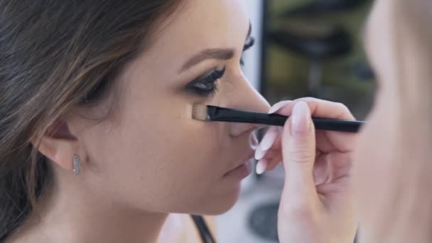 Close-up shot van de Visagist maakte de avond make-up van haar model, dan de concealer opnieuw het neemt en het met een borstel onder de ogen van de klanten zet, corrigeert de fouten van het oog make-up. — Stockvideo
