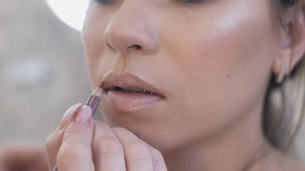 Close-up, cropped frame, make-up artist paints the clients lips with a nude pencil, blends color, outlines the contour of plump lips. Girl has a healthy beautiful skin, rich lips, brings them. — Stock Video