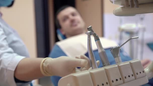 Equipamentos médicos, dentistas ferramentas na clínica em primeiro plano. O médico pega a máquina e realiza os procedimentos com o paciente em segundo plano. Clínica odontológica, conceito de saúde — Vídeo de Stock