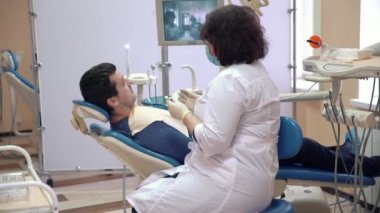 Bir erkek hasta bir klinik diş bir sandalyede yatıyor ve istişare bir dişçi alır. Doktor diş inceler ve yordamlar ve tedavi gerçekleştirmek hazırlar.