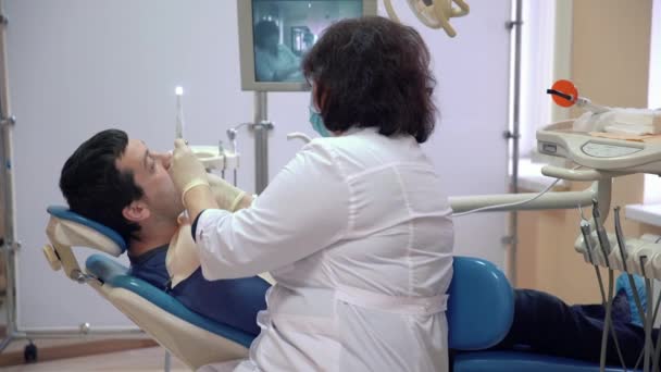 La donna dentista tratta i denti al paziente. Un uomo si trova su una sedia in una clinica dentale . — Video Stock