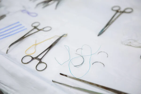 Instrumentos quirúrgicos de primer plano en una mesa médica en una clínica durante la cirugía. Tijeras metálicas estériles, pinza, aguja quirúrgica en la mesa o en la mano del médico. El concepto de salud, herramientas . — Foto de Stock