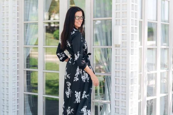 Sonriente chica de moda en ropa de seda, esperando a sus amigos en la terraza del restaurante, quiere reunirse lo antes posible. La mujer tiene un aspecto europeo, cabello oscuro, dientes blancos — Foto de Stock