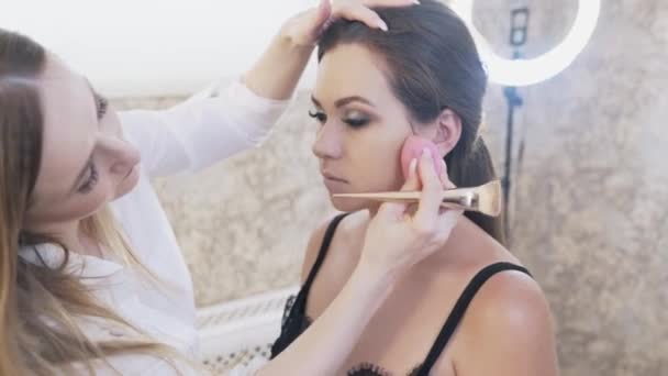 Närbild av en skönhetssalong cleat sitter på en stol med en make-up artist med sotade ögon makeup, de flicka skjuter modellerna hud med svamp, korrigerar fel av makeup. — Stockvideo