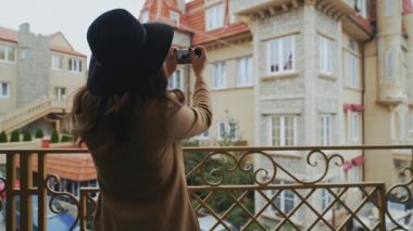 Görünümü arka, yakın çekim, steadikam ince kadın palto ve şapka şehir etrafında yürür, onun Smartphone'da mimar bir fotoğrafı çeker, bir yürüyüş sahiptir. Kızım hafta sonu Avrupa'ya uçtu.