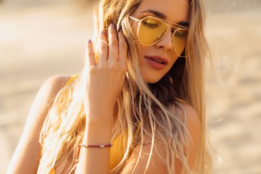 Yakın çekim portre sarı mayo ve plaj güneş gözlüğü seksi bir kız. Kalıcı makyaj ve güzel saç modeli ile inanılmaz kadın yüzü. Model tatil, seyahat ve sunbathes.