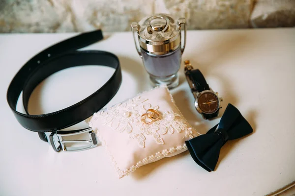 Мужские аксессуары, кожаный ремень, духи, галстук-бабочка, золотые кольца жениха, часы и невесты на белом столе. Концепция одежды для бизнесменов . — стоковое фото