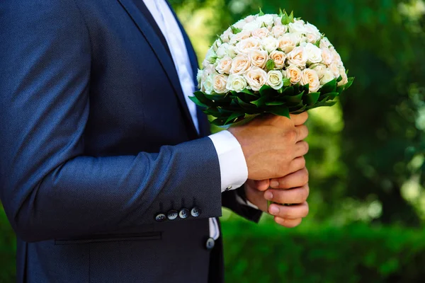 Primo piano di una cornice ritagliata è un tenero mazzo di rose nelle mani dello sposo. Un uomo in abito da sposa tiene dei fiori. . — Foto Stock