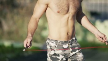 Ağır çekim, kamuflaj atlet spor alanında bir atlama ipi ile atlar pantolon. Kaslı adam spor egzersizleri yapmadan önce ısınma. Fitness kavramı, sağlık. Yakın çekim gövde.