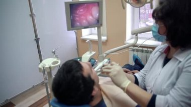 Bir kadın dişçi bir hasta diş içi sözlü bir fotoğraf makinesi ile inceler ve sonuçları monitörde görüntüler. Tedavi ve korunma diş hastalıkları, çürük, sağlık kavramı.