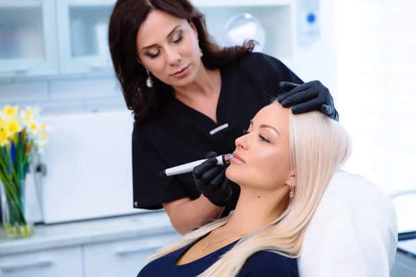A mão de cara e cosmetologist de mulheres de close-up executa procedimentos na cara de pacientes com um aparelho hidro-peeling. Limpeza e rejuvenescimento da pele de mulheres com novas tecnologias . — Fotografia de Stock