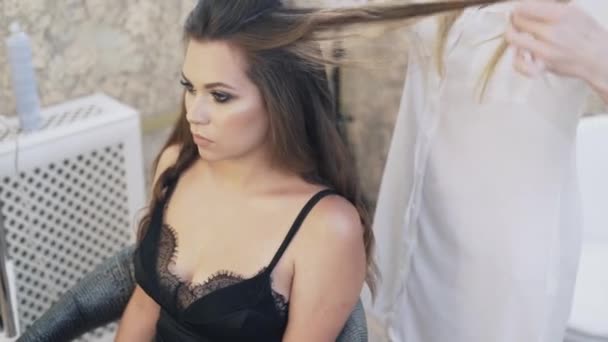 Een close-up, bijgesneden frame, een mooie jonge brunette met een diepe hals zit in een stoel kappers, doet haar kapsel met haar stylist. — Stockvideo