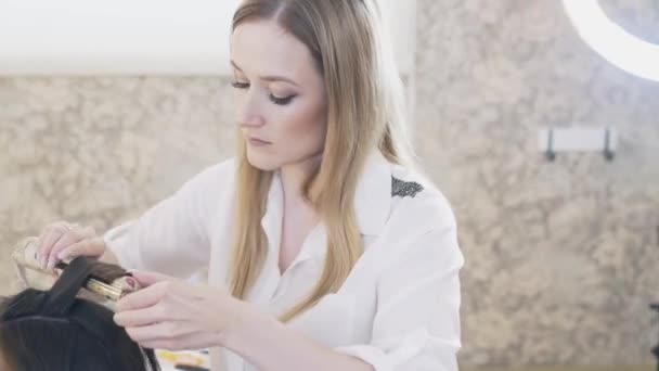 Närbild, stylist verk i hennes skönhetssalong, en make-up artist, Frisör gjorde en kväll make-up för klienten, och gör en wrap, vindar hennes klienter långt hår med tång. — Stockvideo