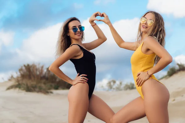 Couple of sexy girls posing at the beach, show the heart symbol with their hands. — Stock Photo, Image