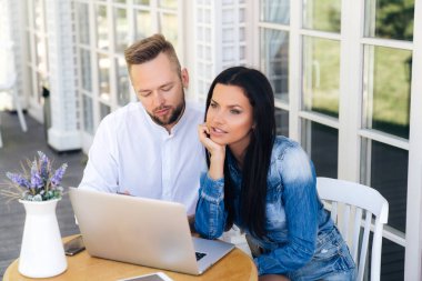 En iyi görünüm güzel bir genç çiftin bir dizüstü bilgisayar kullanarak dışında masadan. Adam onun telefon sms okuyor, geçen arabalara düşünceli görünüyor. Gadget'ları kavramı