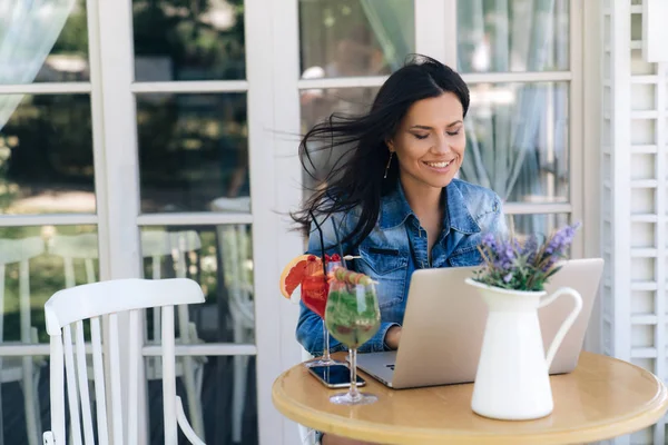 Eine glückliche junge Frau arbeitet im Internet, sitzt an einem Tisch in einem Café und kauft online ein, hat gerade per Bankkarte über das Internet einen sehr begehrten Einkauf bezahlt. — Stockfoto