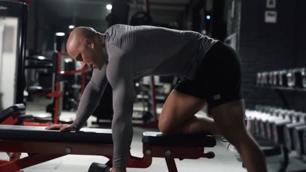 Muskulös man i sport träning i gymmet med hantlar utför övningar på ryggmusklerna — Stockvideo