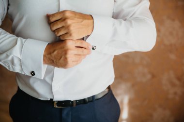 Closeup işadamı kol düğmesi koyar, pahalı deri kemer takıyor. Bir iş takım elbise, Beyaz tişörtlü adam. Damat düğün gününde hazırlanıyor