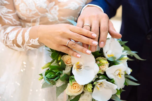 Close-up das mãos dos recém-casados com anéis de casamento, toque suavemente o buquê de casamento de flores — Fotografia de Stock