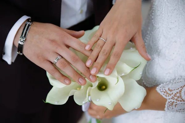 Крупный план рук молодоженов с обручальными кольцами, нежно коснуться свадебного букета цветов — стоковое фото