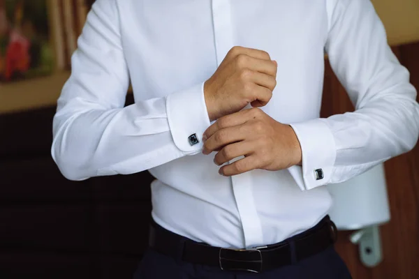 Closeup επιχειρηματίας βάζει μανικετόκουμπα, φοράει ακριβό δερμάτινη ζώνη. Ο άνθρωπος σε ένα business κοστούμι, λευκό πουκάμισο. Προετοιμασία του γαμπρού την ημέρα του γάμου — Φωτογραφία Αρχείου