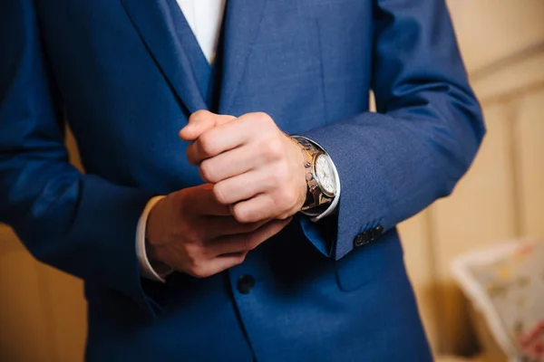 Крупным планом мужчина надевает золотые часы с кожаным ремнем, бизнесмен одет в стильный костюм, белую рубашку . — стоковое фото