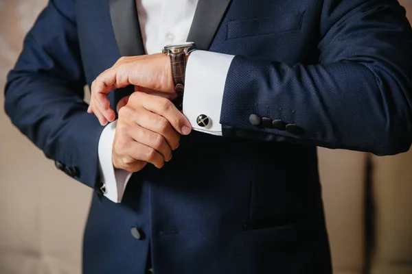 Крупным планом мужчина надевает золотые часы с кожаным ремнем, бизнесмен одет в стильный костюм, белую рубашку . — стоковое фото