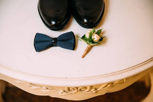 Mens leather shoes, bow tie and boutonniere on a white table background. Clothing accessories businessman.