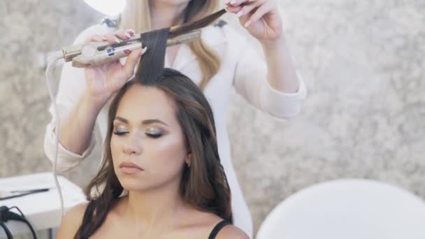 Närbild, stylist verk i hennes skönhetssalong, en make-up artist, Frisör gjorde en kväll make-up för klienten, och gör en wrap, vindar hennes klienter långt hår med tång. — Stockvideo