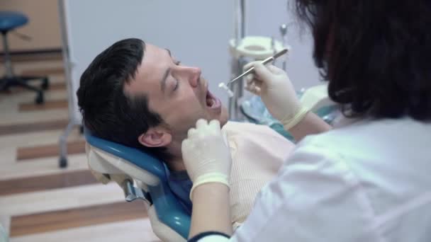 Uma mulher dentista em uma máscara estéril e roupas realiza procedimentos na boca pacientes com instrumentos médicos. Tratamento dentário numa clínica dentária. Conceito de saúde . — Vídeo de Stock