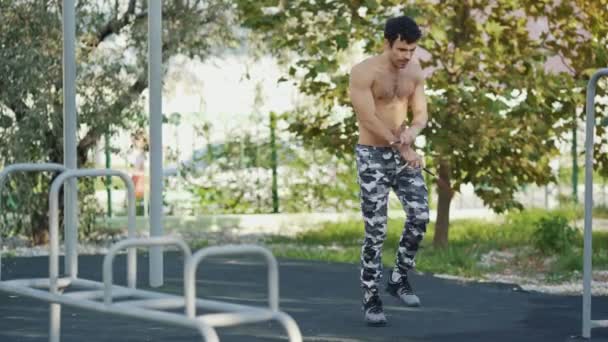 Joven atleta salta con una cuerda de saltar en el campo de deporte en el parque de verano — Vídeos de Stock