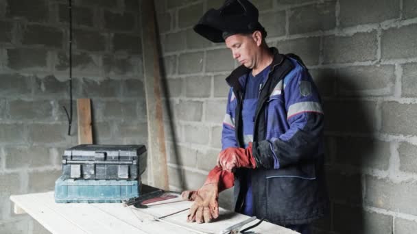 Soldador se pone guantes rojos, soldadores casco y comienza a trabajar . — Vídeos de Stock