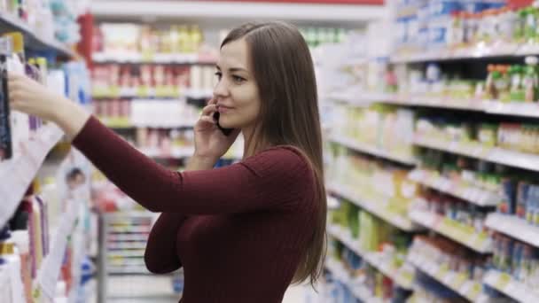 Hezká brunetka mluví o telefonu a volba něco v supermarketu. — Stock video