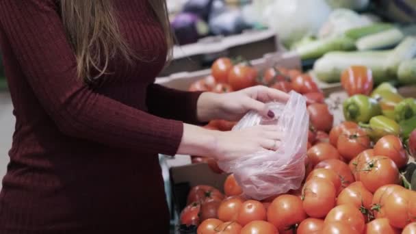 Close up mulher coloca tomates em saco de plástico de balcão com legumes frescos . — Vídeo de Stock