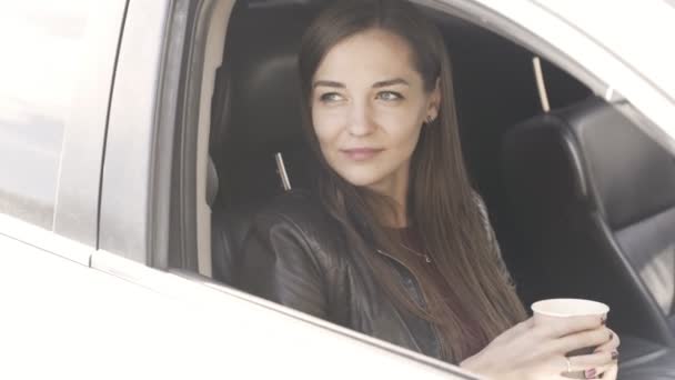 Young beautiful caucasian female sitting in car and holding coffee in her hands. — Stock Video